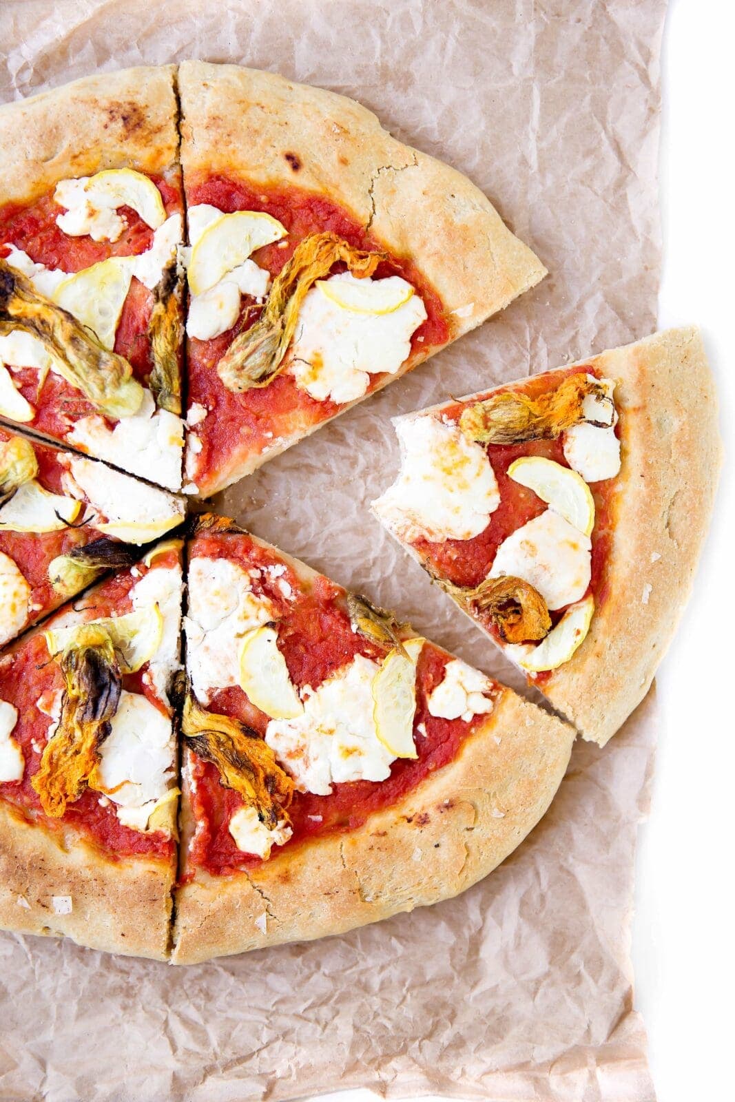 A perfect summer pizza made with crushed tomatoes, mozzarella, and squash blossoms!