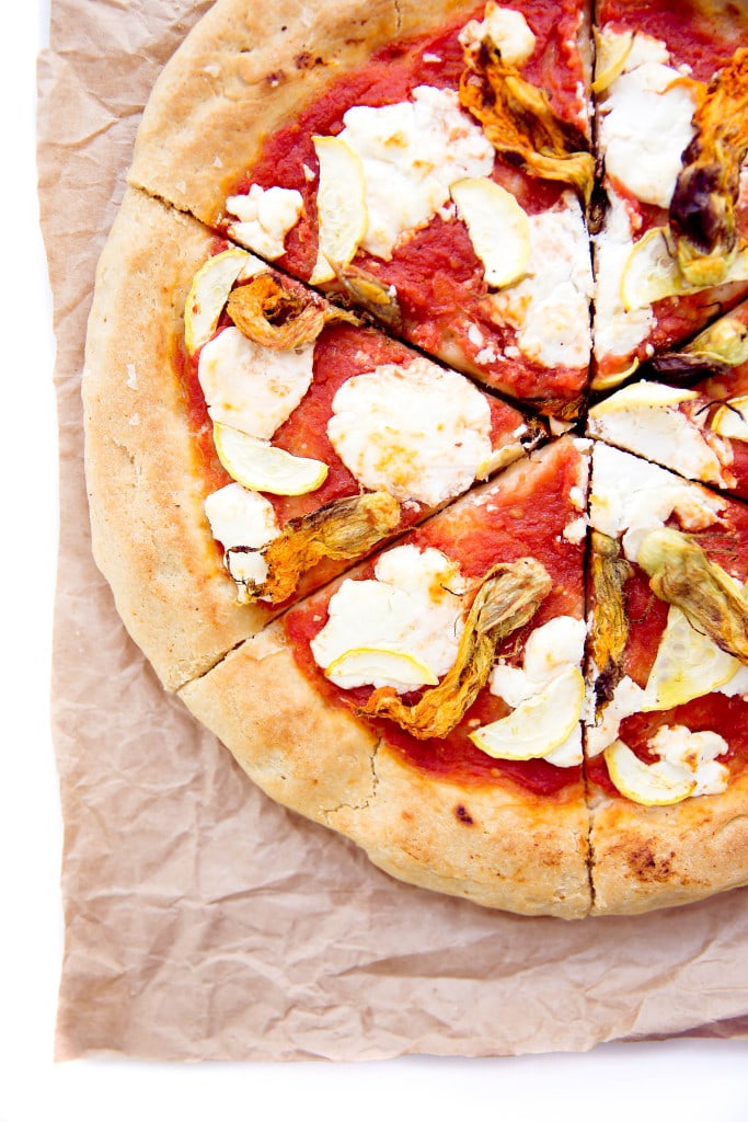 A perfect summer pizza made with crushed tomatoes, mozzarella, and squash blossoms!