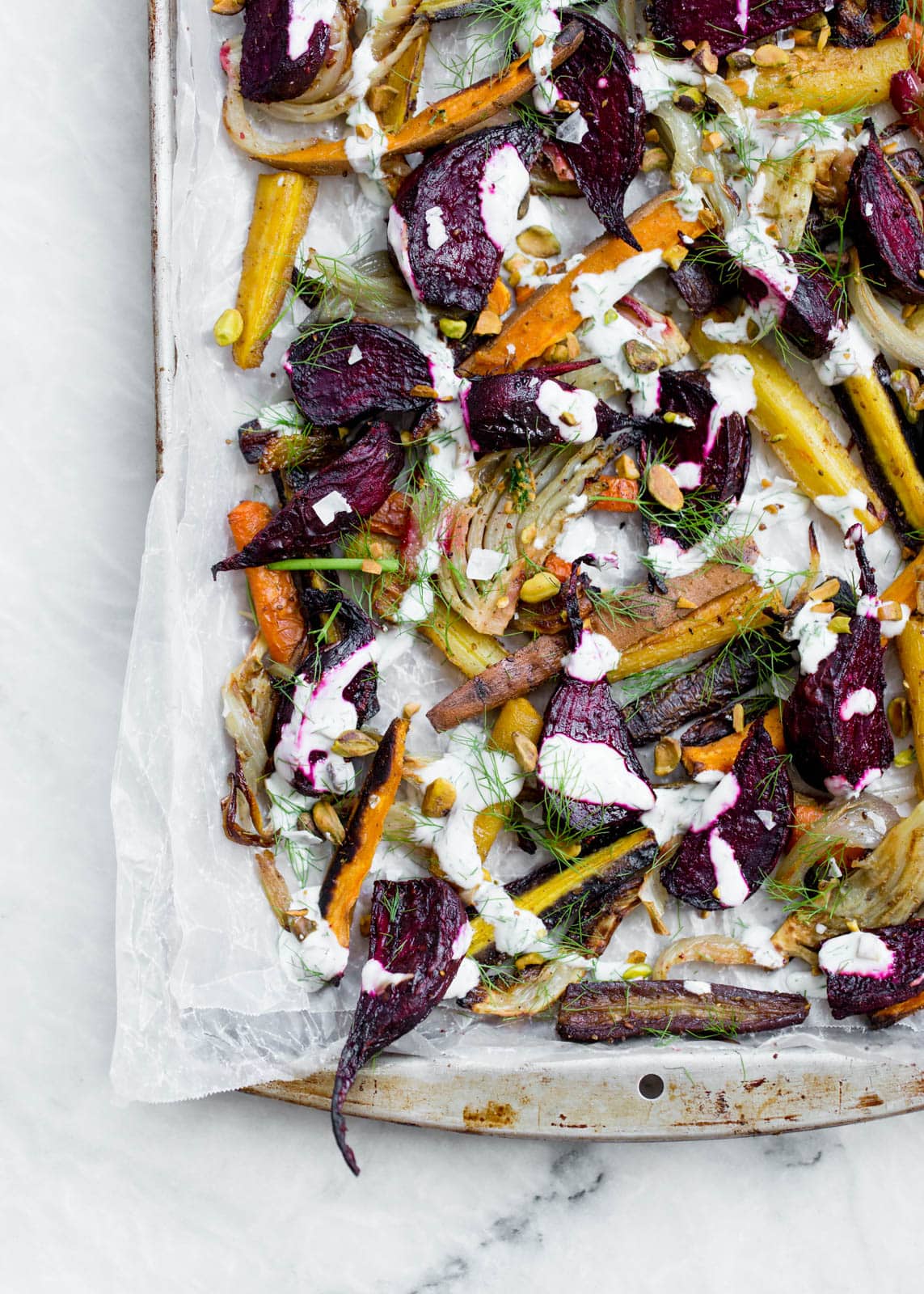 Perfectly caramelized Roasted Root Vegetables tossed in fennel and cumin and drizzled with pistachio yogurt and fennel fronds.