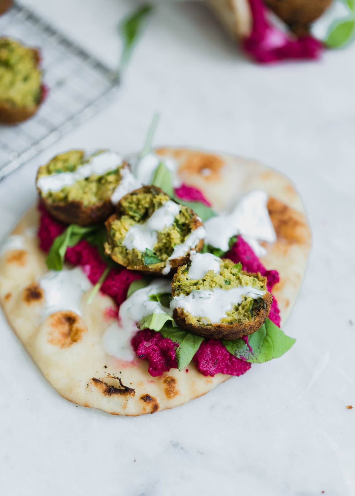 green falafel sandwich drizzled with yogurt sauce