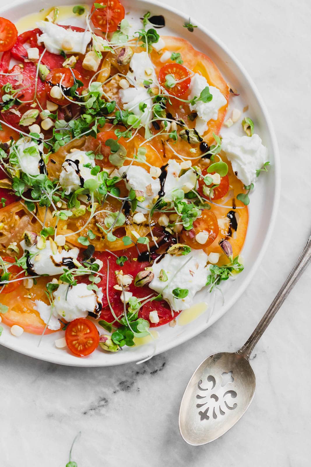 A raw Heirloom Tomato Carpaccio made with thinly sliced heirloom tomatoes, fresh burrata cheese, pistachios, corn, and microgreens.