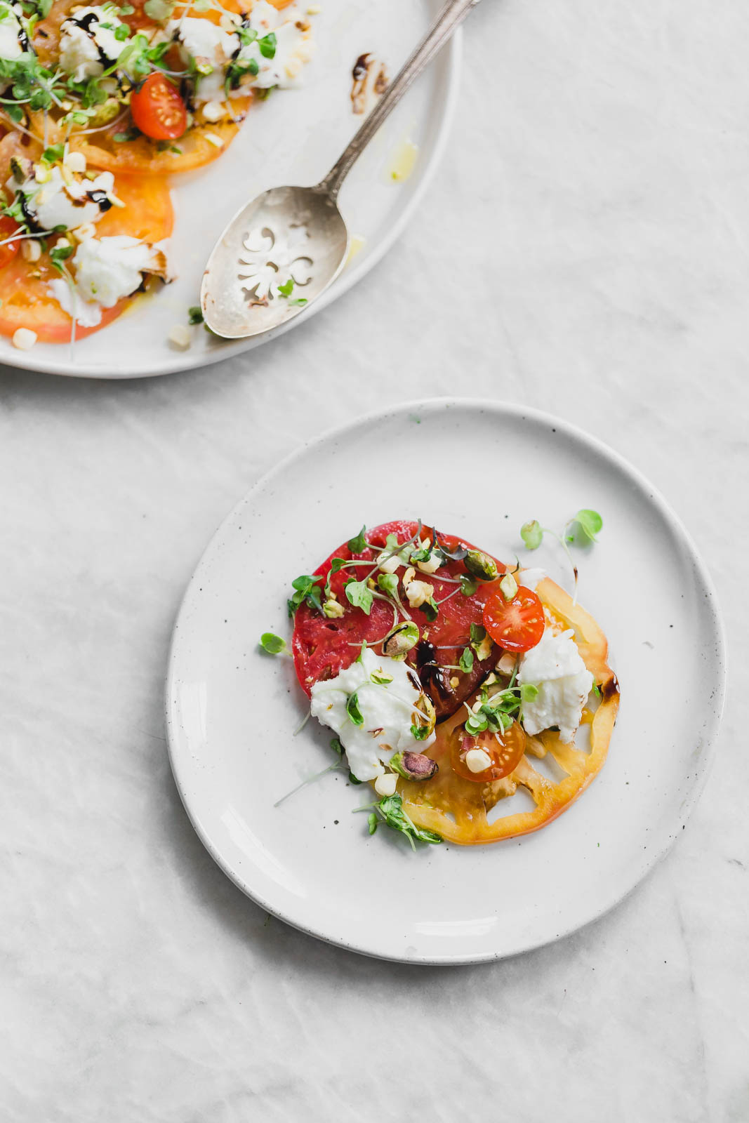 A raw Heirloom Tomato Carpaccio made with thinly sliced heirloom tomatoes, fresh burrata cheese, pistachios, corn, and microgreens.