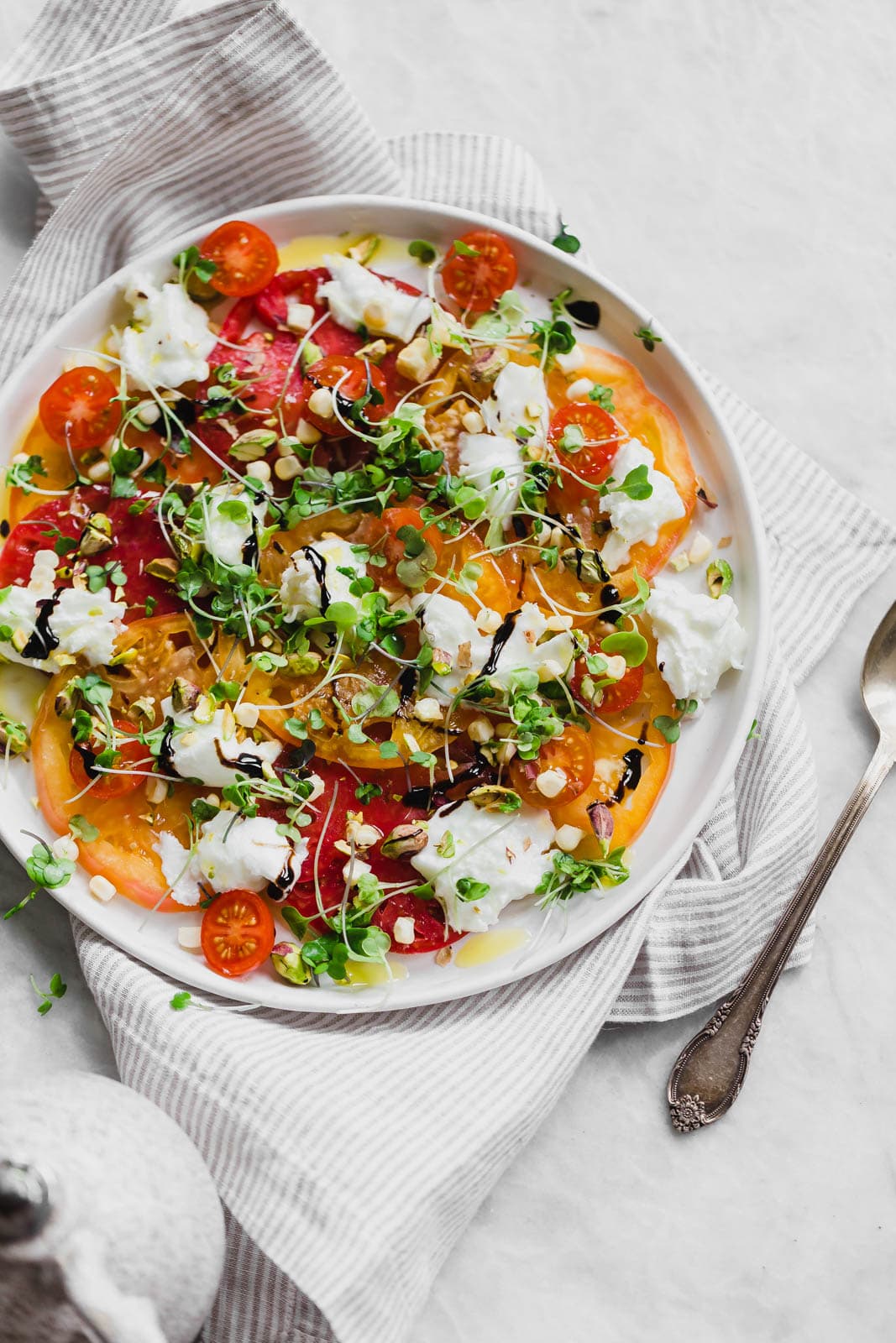A raw Heirloom Tomato Carpaccio made with thinly sliced heirloom tomatoes, fresh burrata cheese, pistachios, corn, and microgreens.