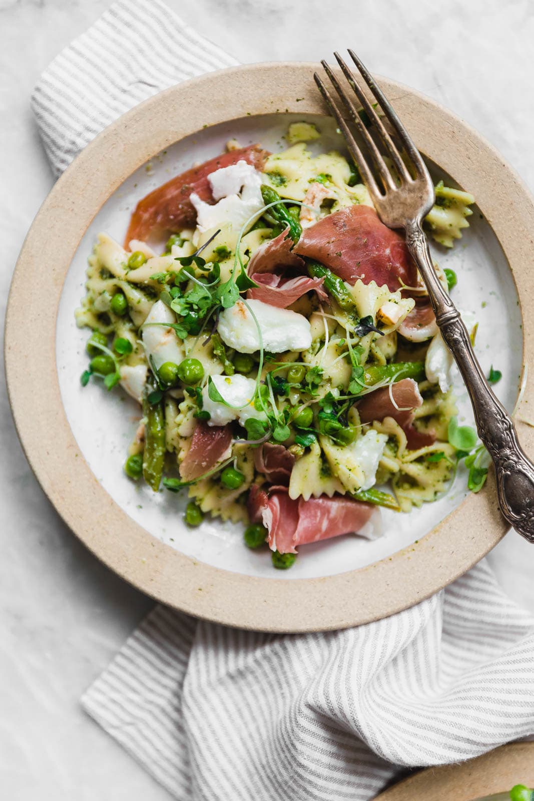 A sensational pasta salad with homemade pesto, prosciutto, peas, asparagus, and burrata.
