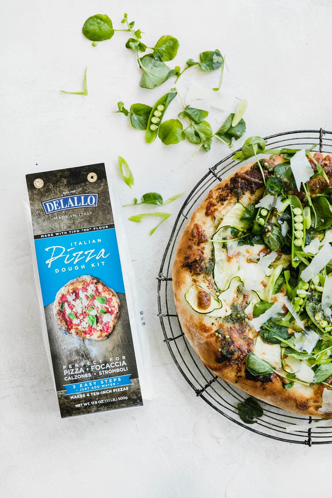 A Spring Green Goddess Pizza made with pesto, zucchini, spring peas, watercress, mozzarella, and a green goddess dressing. 