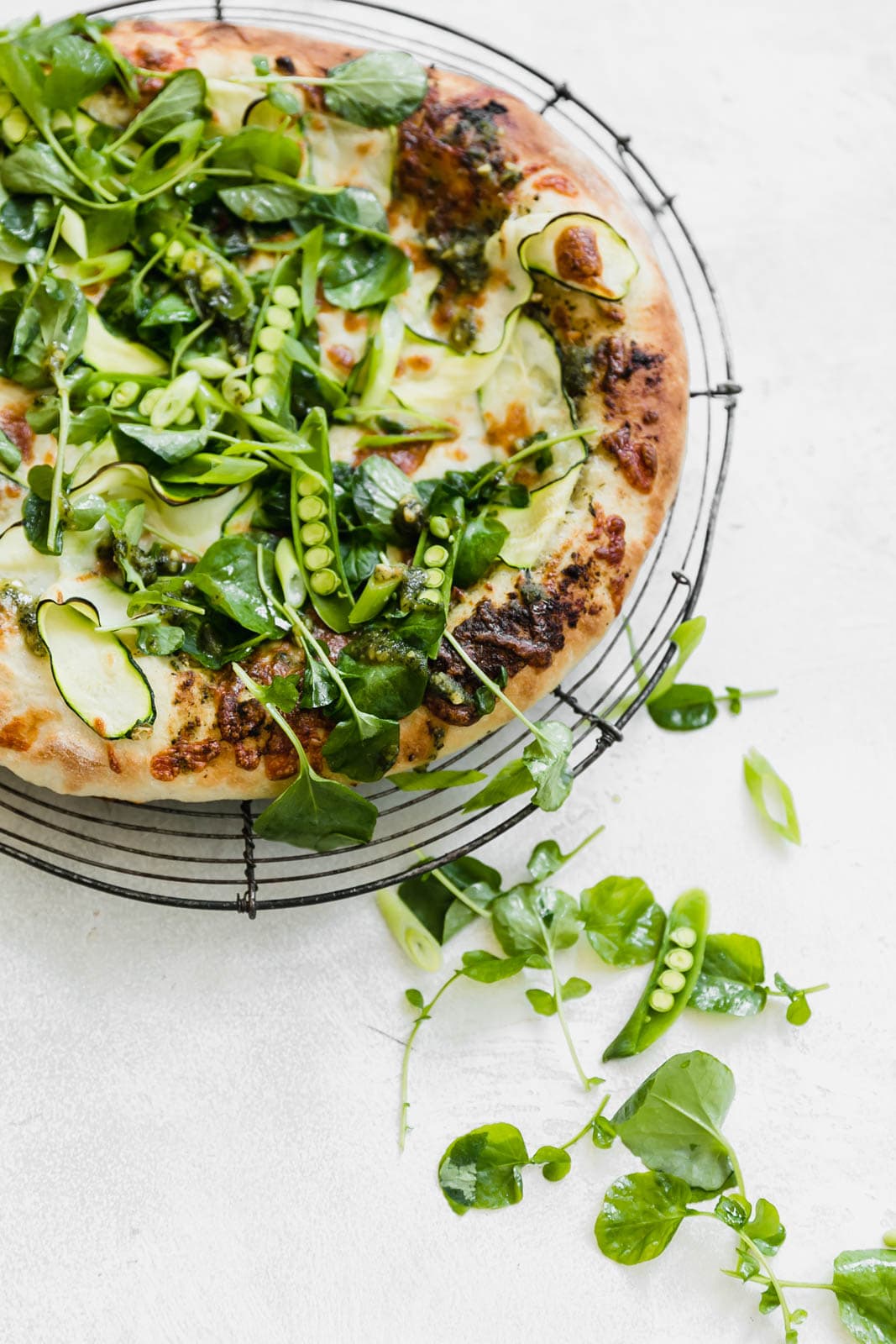 A Spring Green Goddess Pizza made with pesto, zucchini, spring peas, watercress, mozzarella, and a green goddess dressing. 