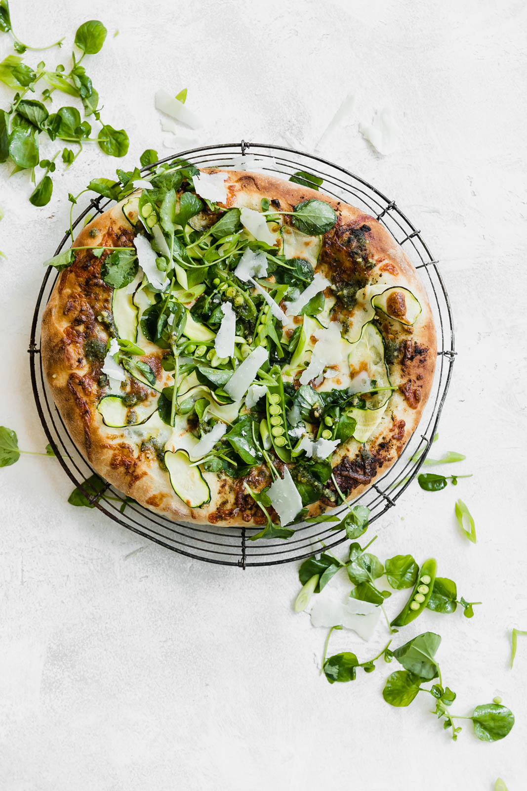 A Spring Green Goddess Pizza made with pesto, zucchini, spring peas, watercress, mozzarella, and a green goddess dressing. 