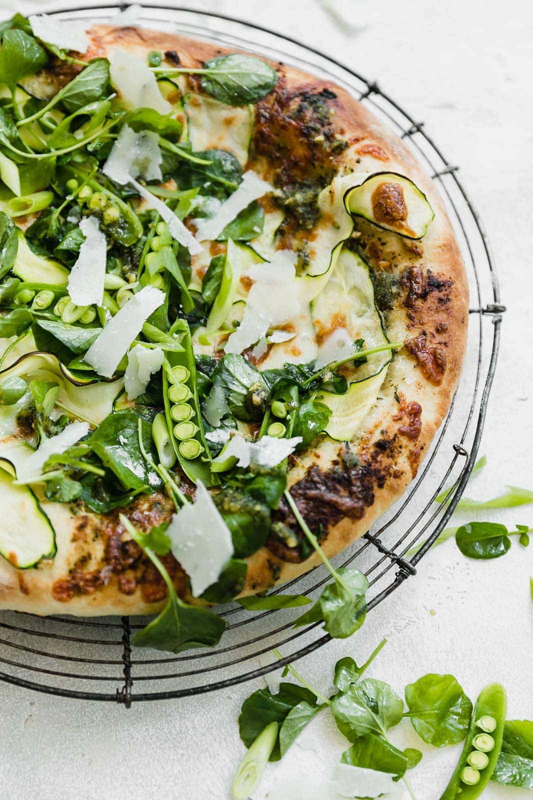 A Spring Green Goddess Pizza made with pesto, zucchini, spring peas, watercress, mozzarella, and a green goddess dressing. 