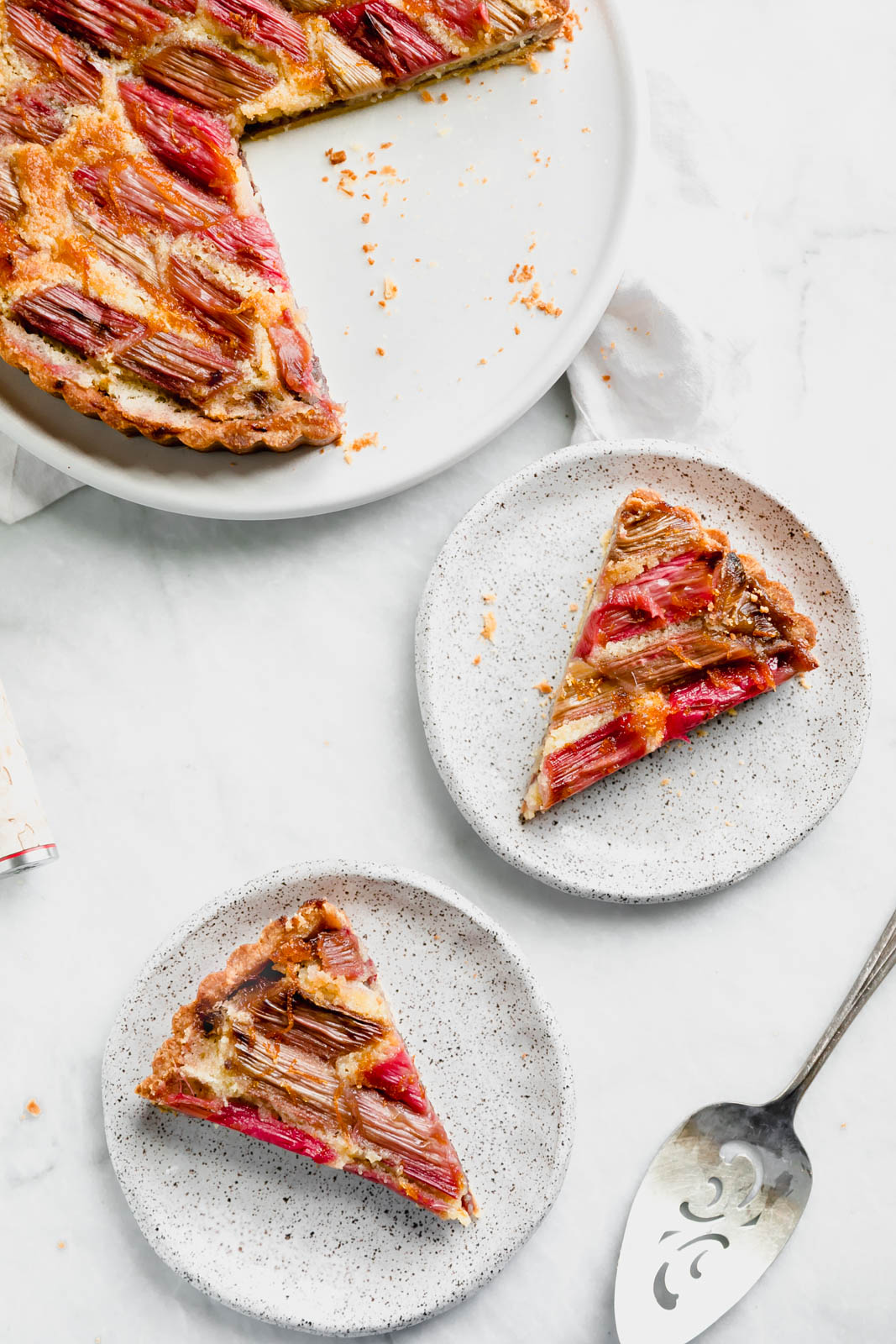 The most showstopping Rhubarb Bakewell Tart made with a pâte sucrée crust, strawberry preserves, almond frangipane, and an orange-soaked rhubarb top