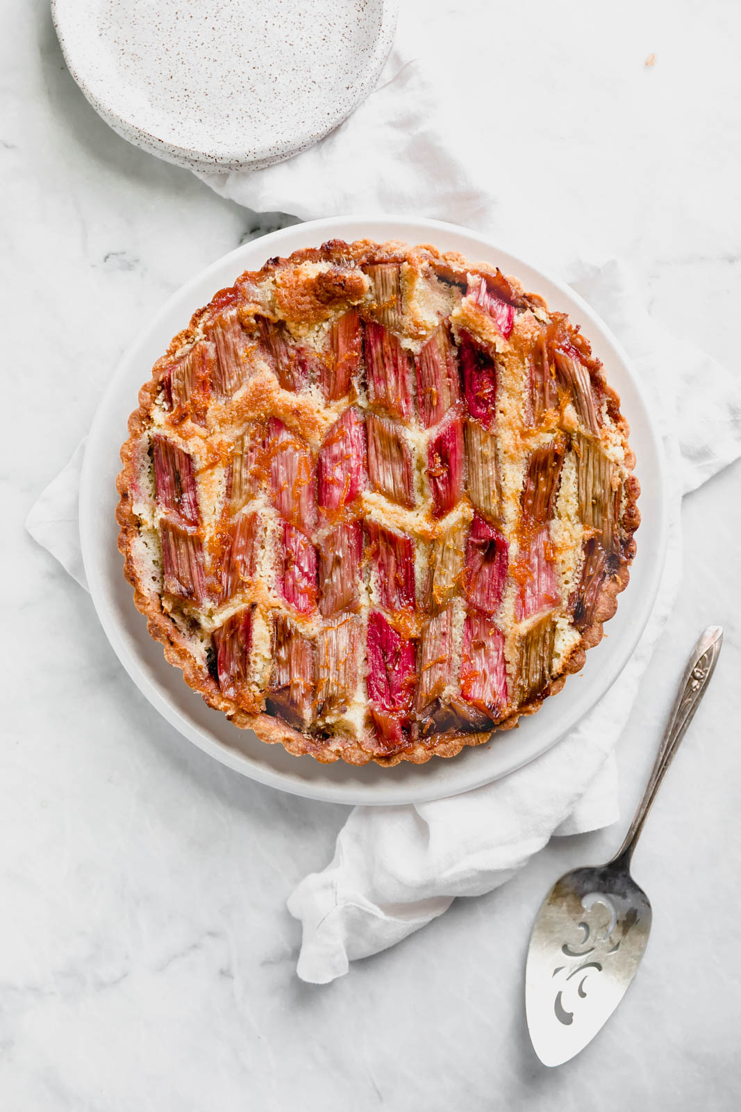 The most showstopping Rhubarb Bakewell Tart made with a pâte sucrée crust, strawberry preserves, almond frangipane, and an orange-soaked rhubarb top