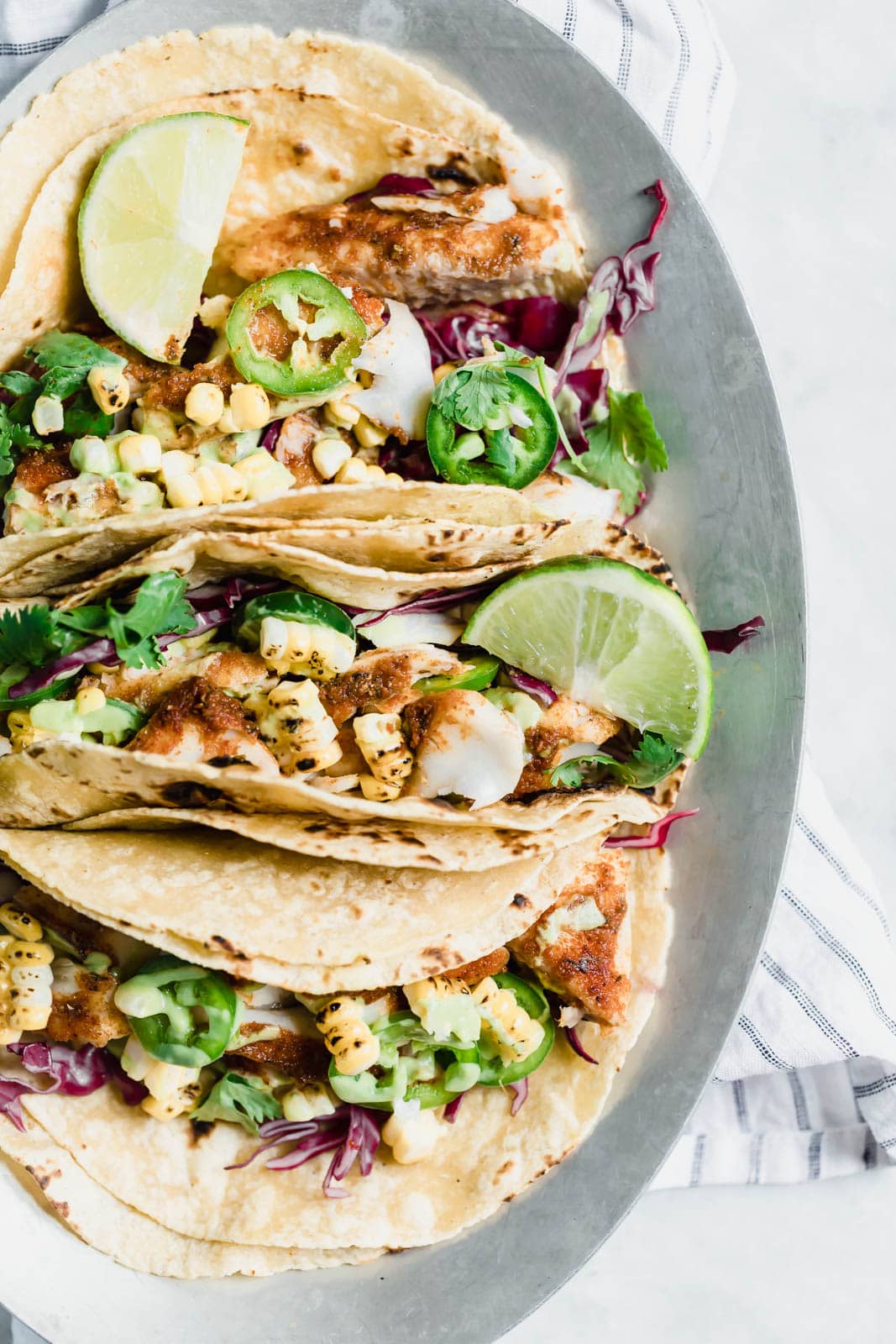 My go-to recipe for Taco Tuesday fish tacos: flakey blackened fish, cabbage, charred corn, jalapeños, and a “creamy” dairy-free avocado cilantro crema!