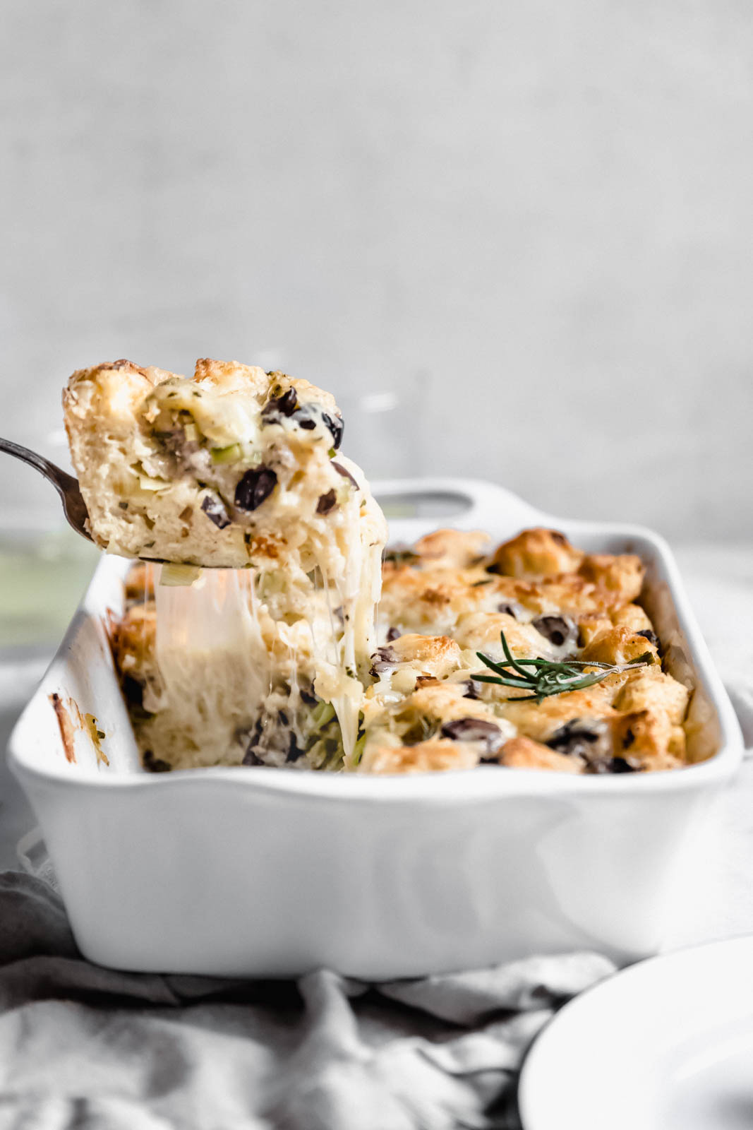 scooping out savory bread pudding from a casserole dish