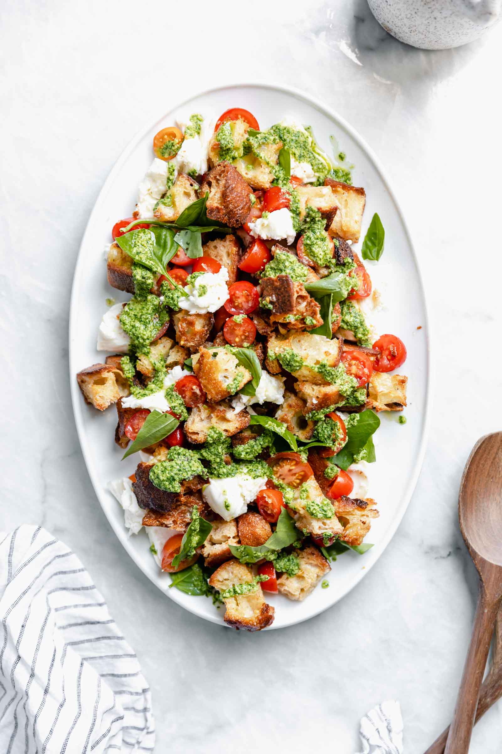 pesto caprese panzanella salad on serving dish with wooden spoon