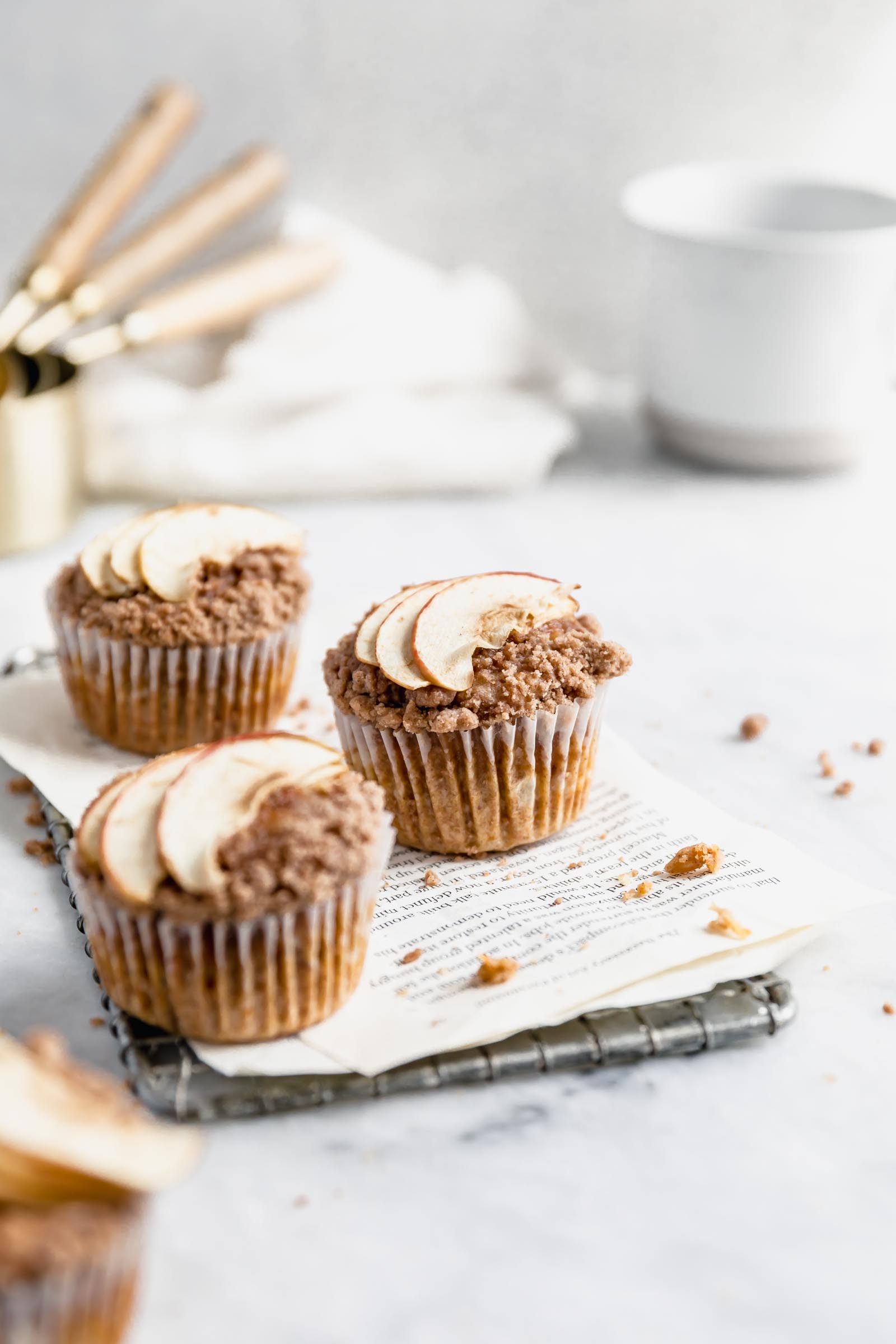 three apple carrot muffins with streusel and sliced apples on a cooling rack