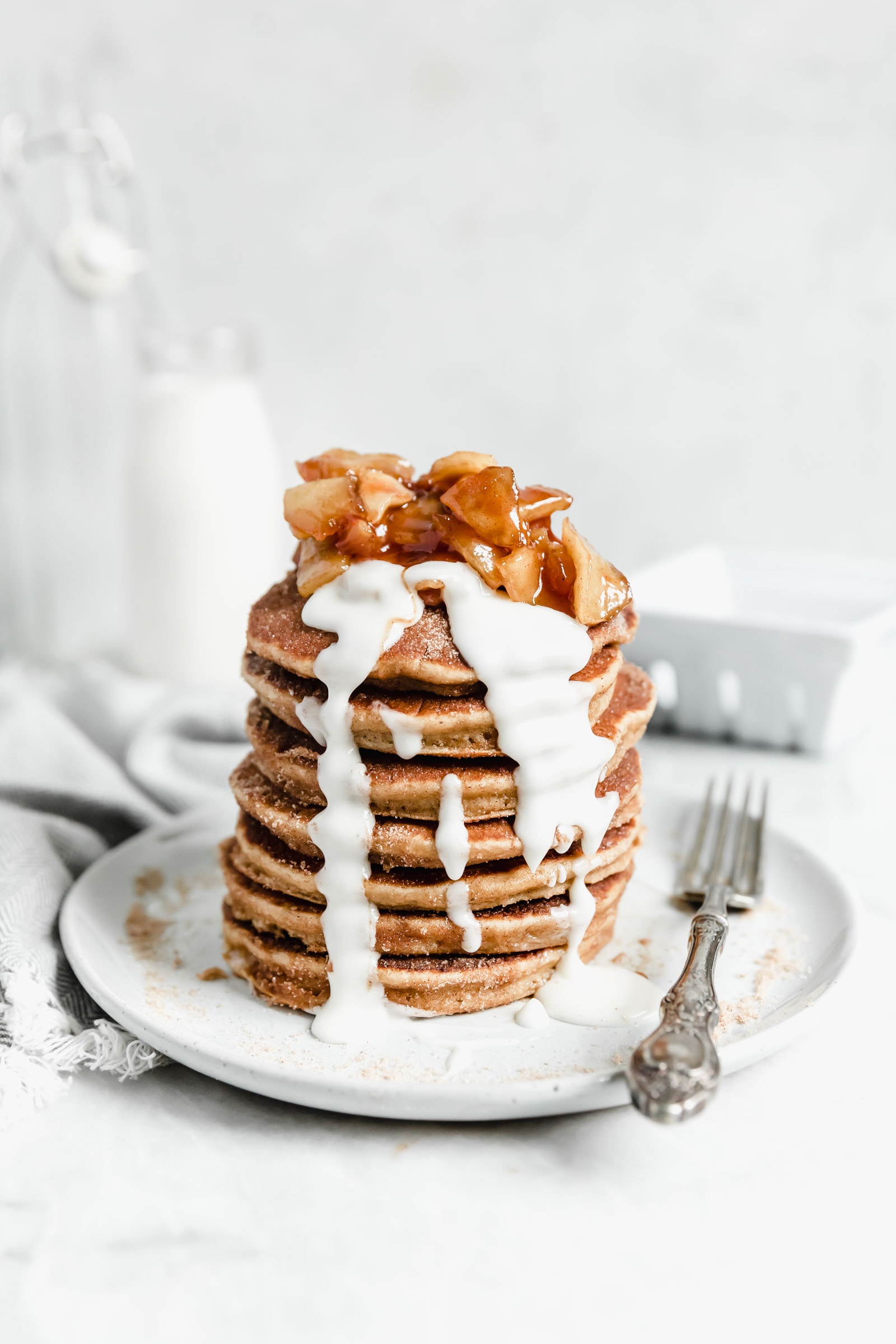 apple donut pancakes drizzled with glaze and topped with cooked apples on a speckled plate