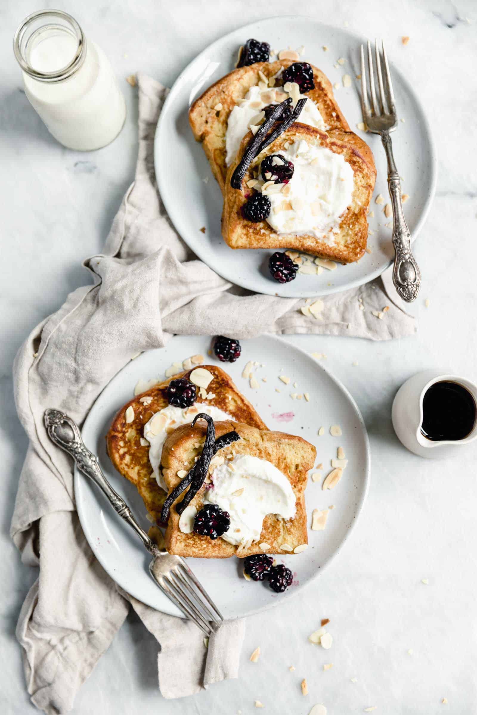 overhead shot of two plates of french toast with whipped cream and berries