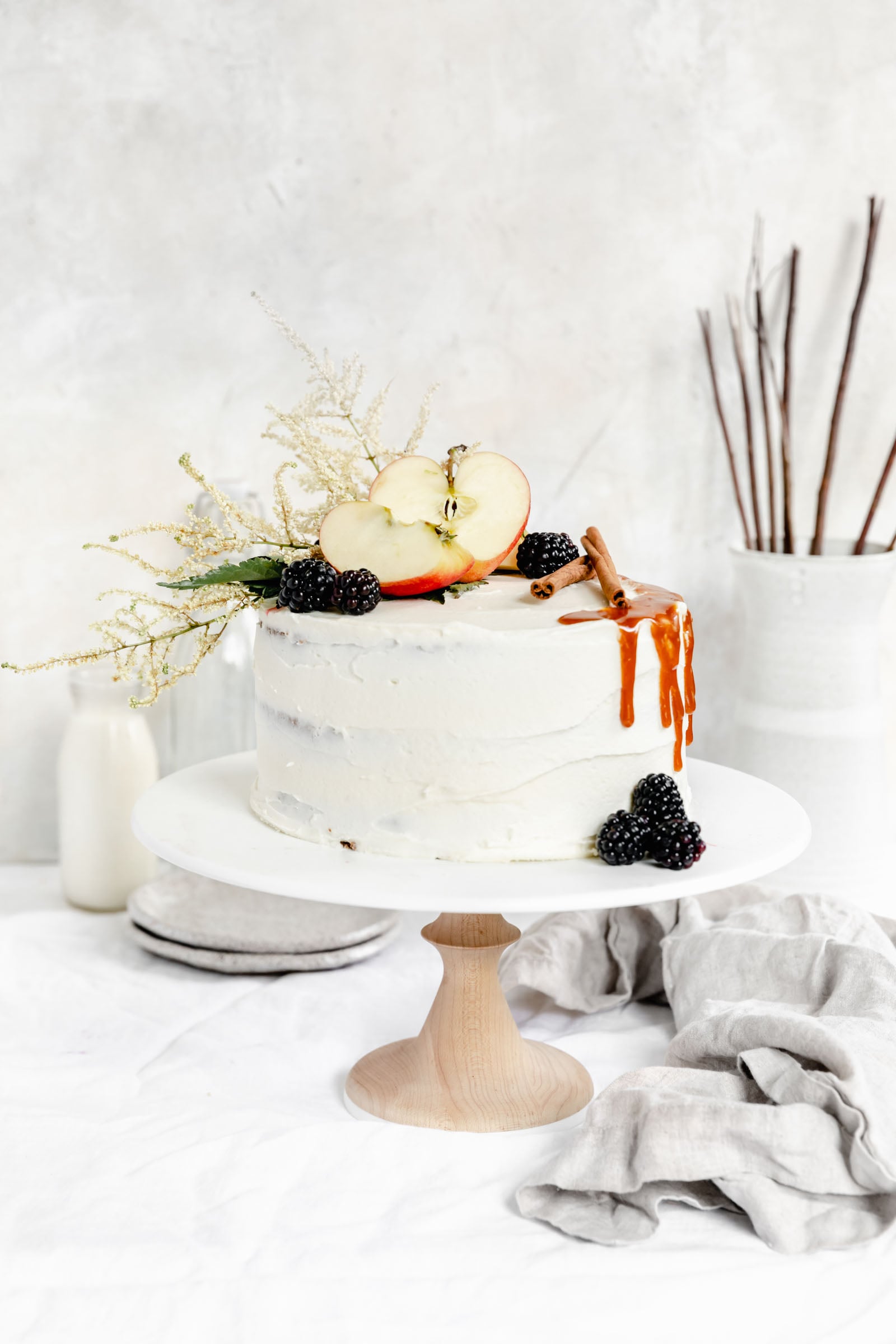 apple cake on cake stand topped with apples, berries and fall flowers