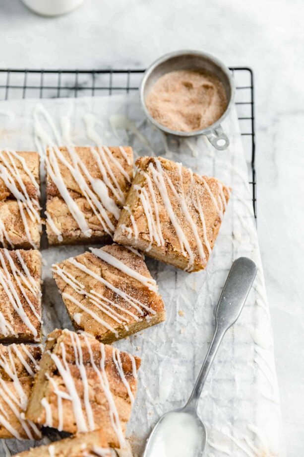 cinnamon roll blondies with cinnamon sugar and spoonful of icing on a cooling rack