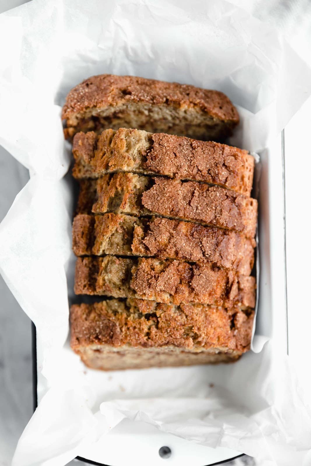 overhead shot of snickerdoodle banana bread in white loaf pan with parchment paper