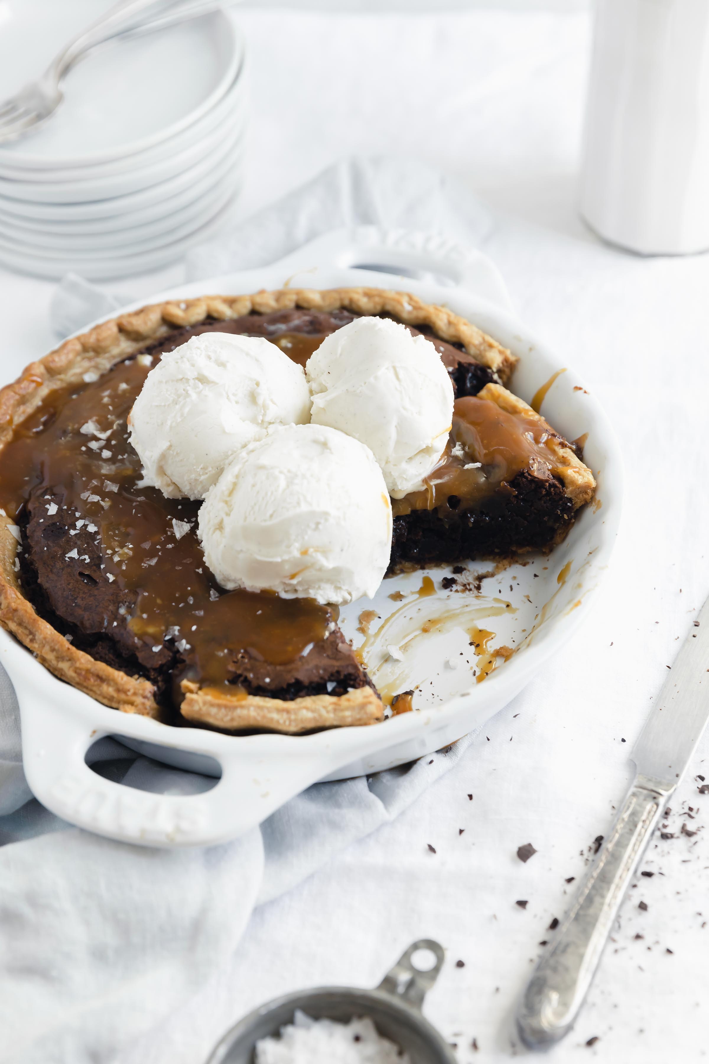 45 degree angle shot of easy salted caramel brownie pie in a white dish with a slice taken out